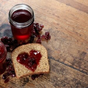 Two jars of fruit jam beside a slice of bread